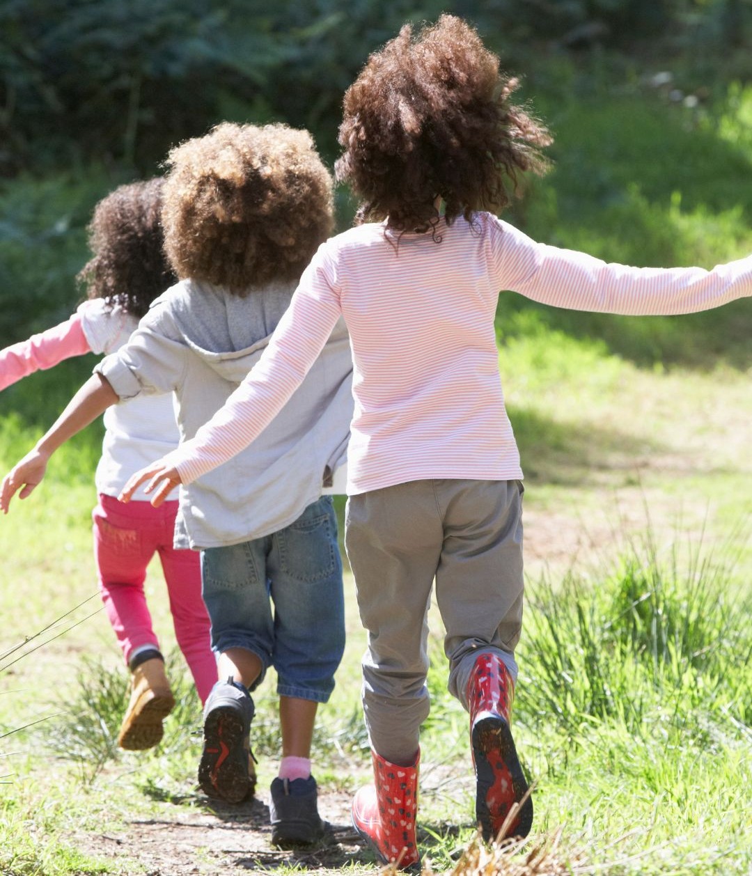 Three children walking in wellies through the long grass