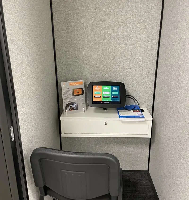 Inside the City Advice Kiosk booth with a small touchpad and leaflets dispenser on a ledge behind a chair.