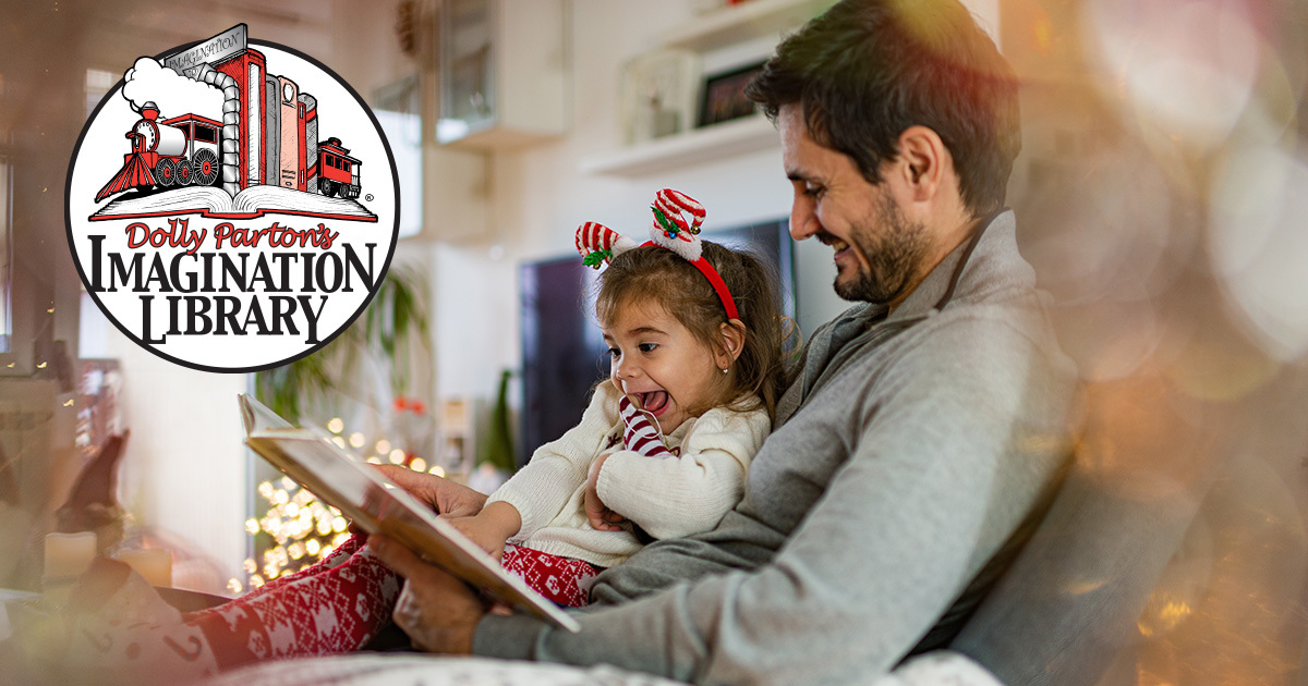 Girl sat on father's lap as he reads her a book
