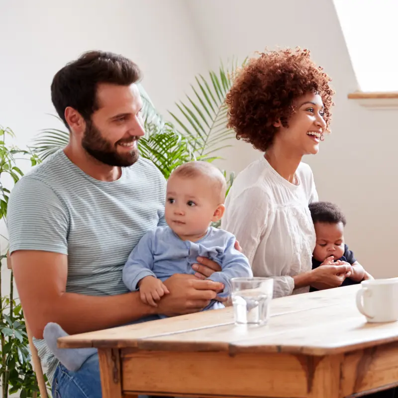 Father and mother sat at table with baby children on their laps