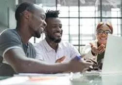 Two men looking at a laptop screen with a woman
